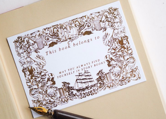 A gold-foiled bookplate with illustrations of knights, dragons, and sea creatures, titled 'This book belongs to' with a space for writing the recipient's name.
