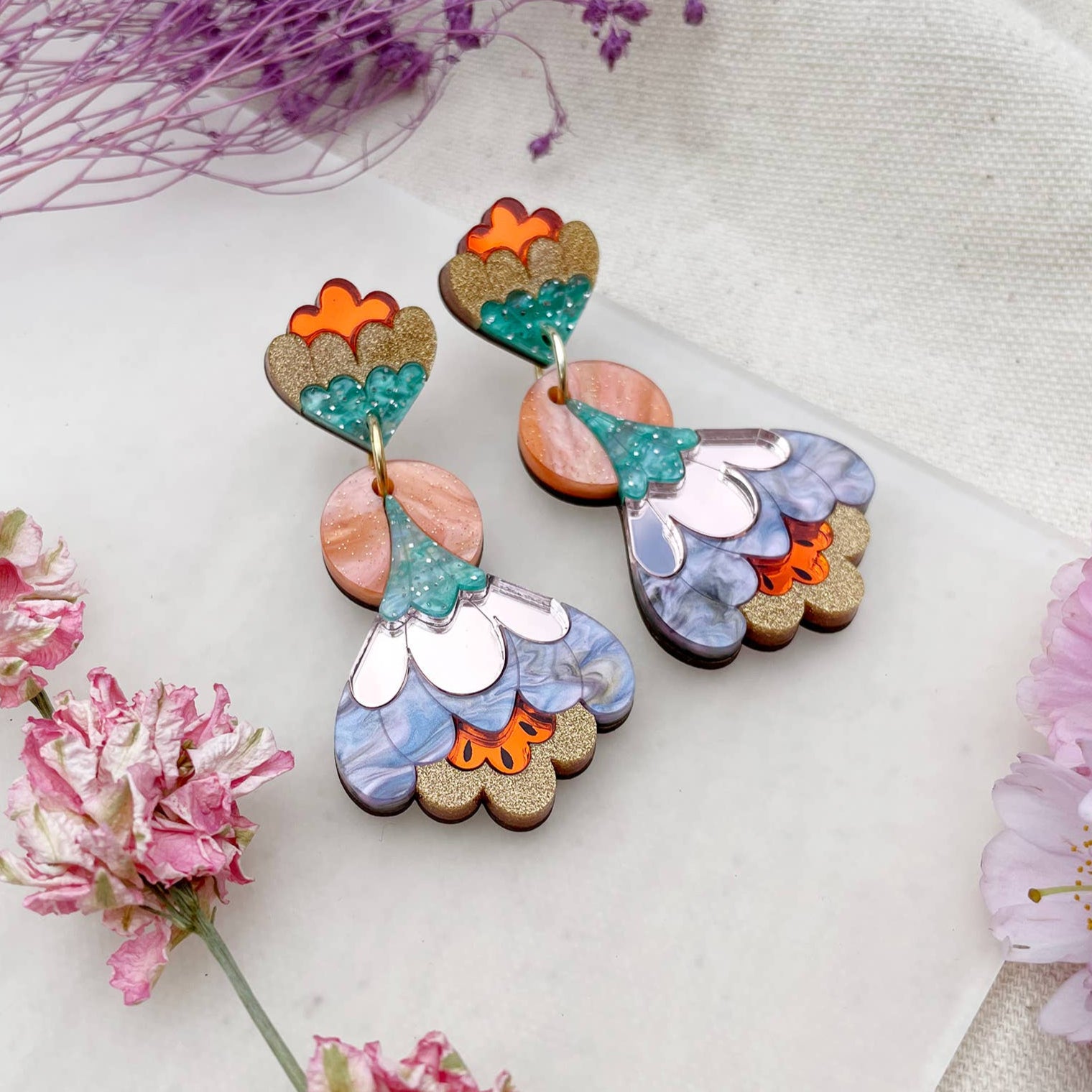 Colorful floral earrings on a white fabric background with pink flowers.