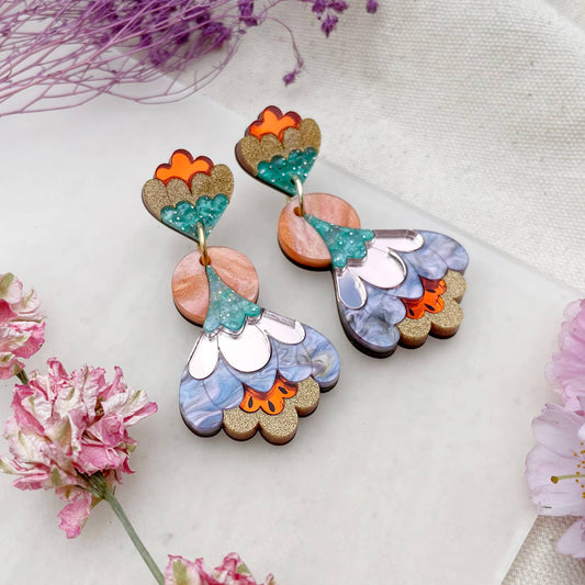 Colorful floral earrings on a white fabric background with pink flowers.