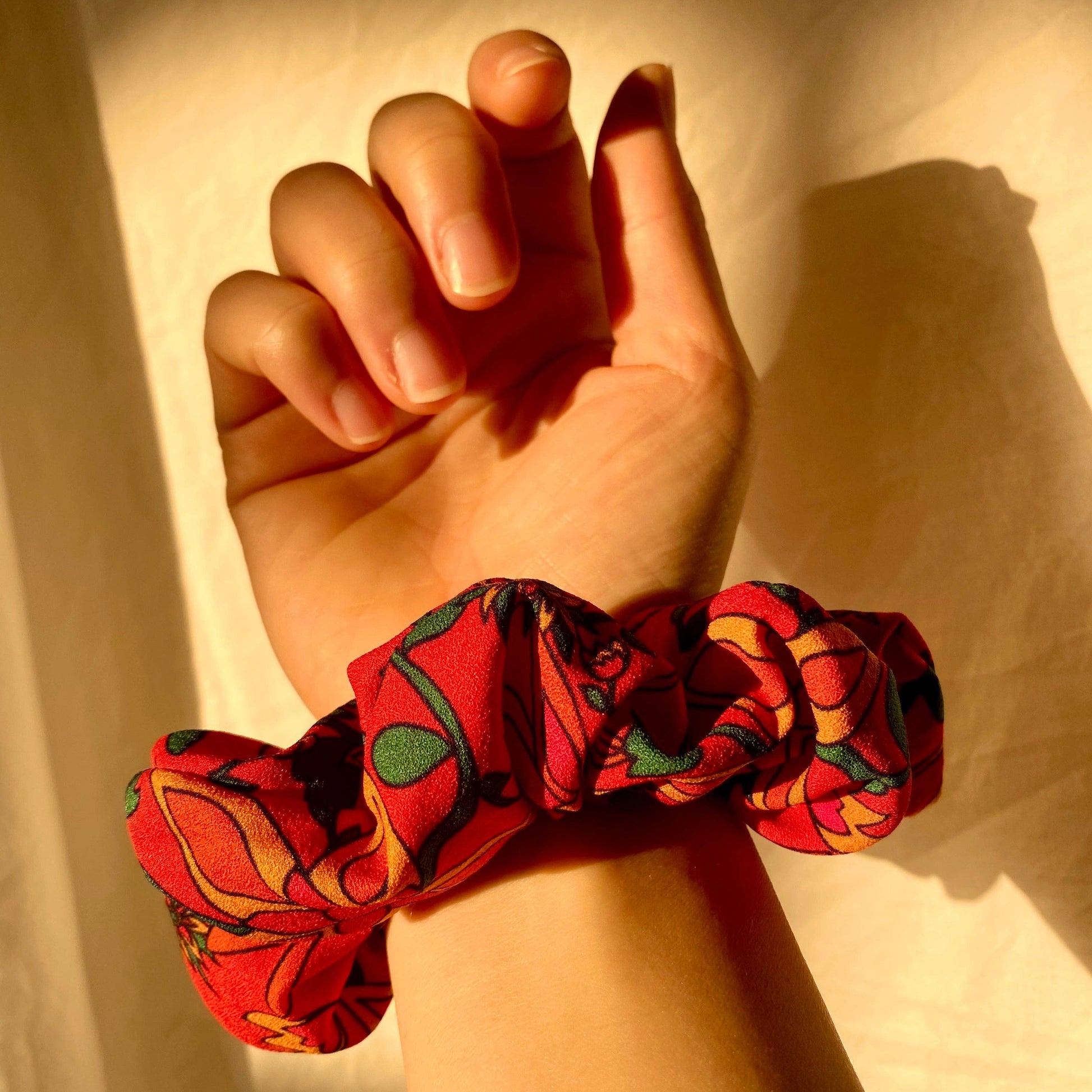 Hand wearing a colorful scrunchie on a plain background