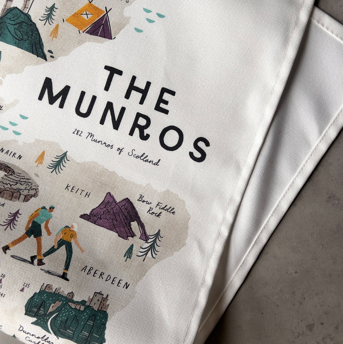 White teatowel with 'The Munros' branding and illustrations on a gray surface