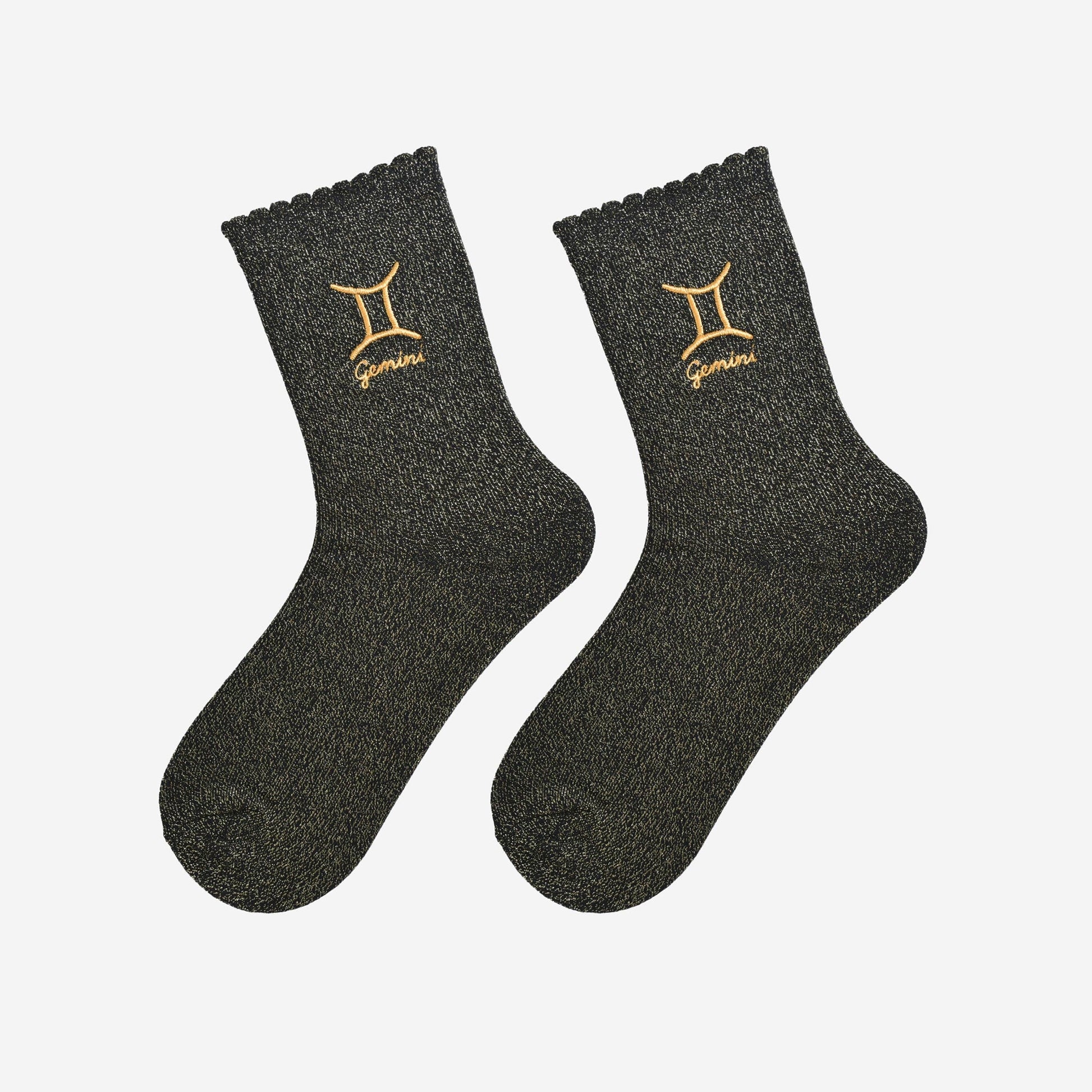 A pair of black socks with gold sparkle and the embroidered gold Gemini star sign lying flat on a white background