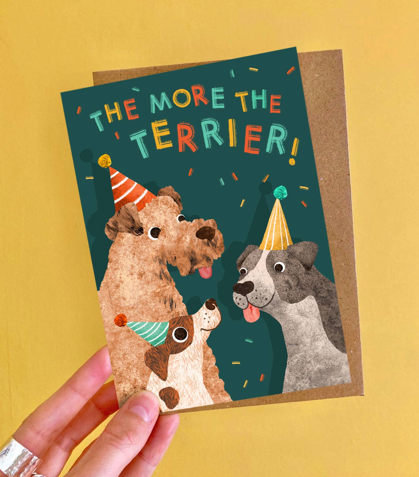 Greeting card with cartoon dogs and 'The More the Terrier!' text on a yellow background