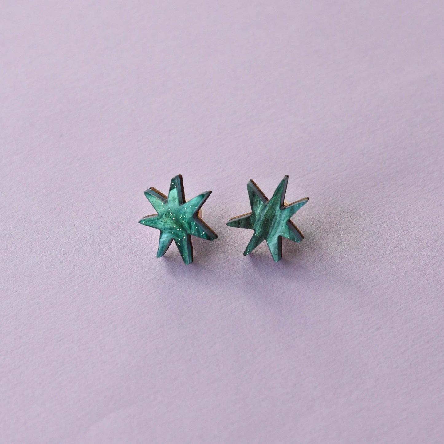 A pair of star-shaped stud earrings with a teal marble effect against a purple background.
