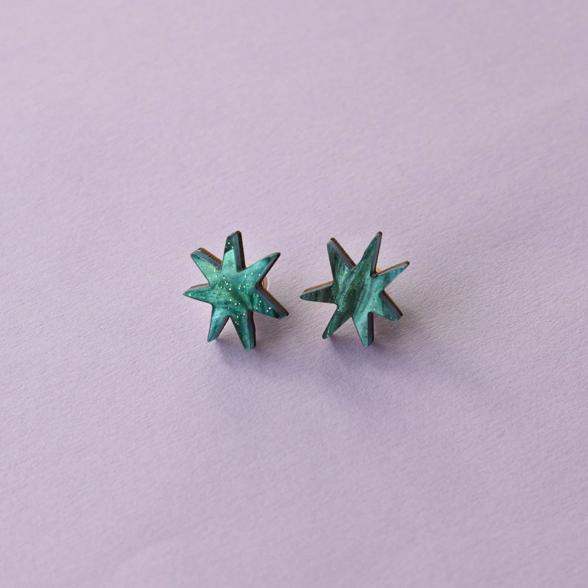 A pair of star-shaped stud earrings with a teal marble effect against a purple background.
