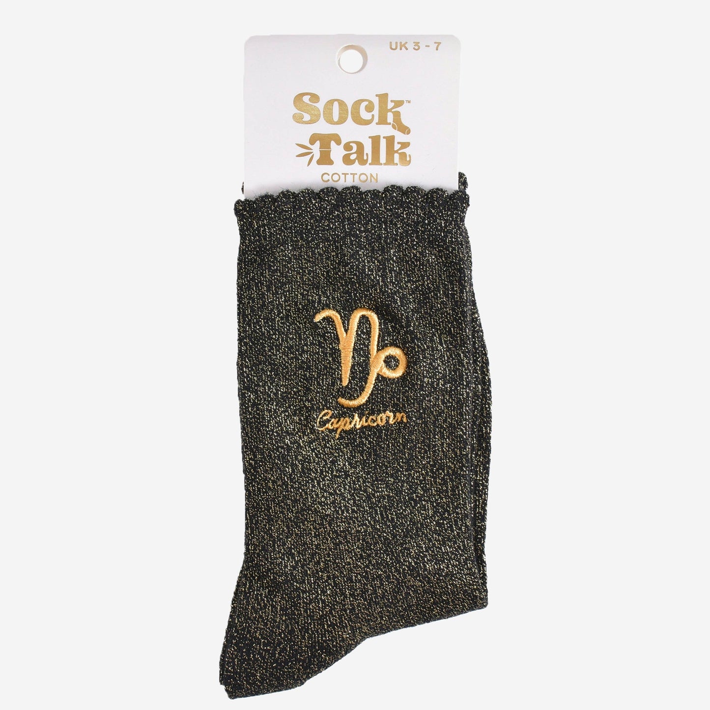 A pair of black socks with gold sparkle and an embroidered gold Capricorn star sign on the ankle area in their packaging