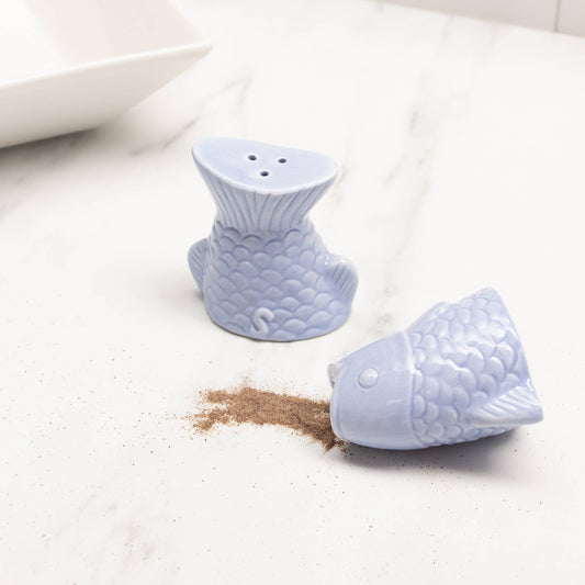 Blue fish-shaped salt and pepper shakers on a white surface with salt spilled out.