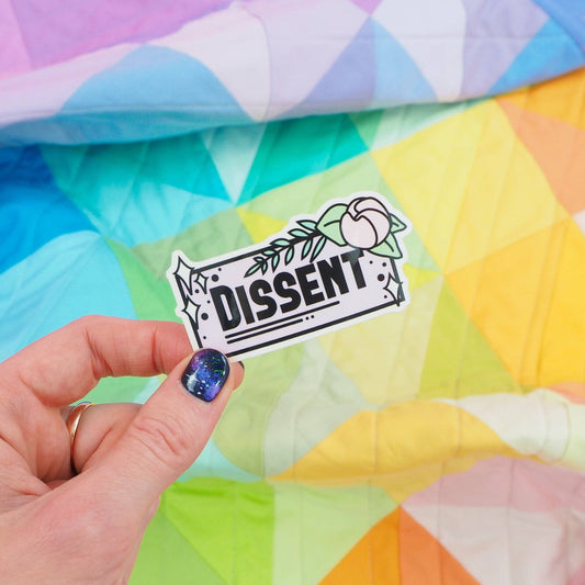A hand holding a vinyl sticker with the word 'Dissent' written on it, against a colorful geometric background.