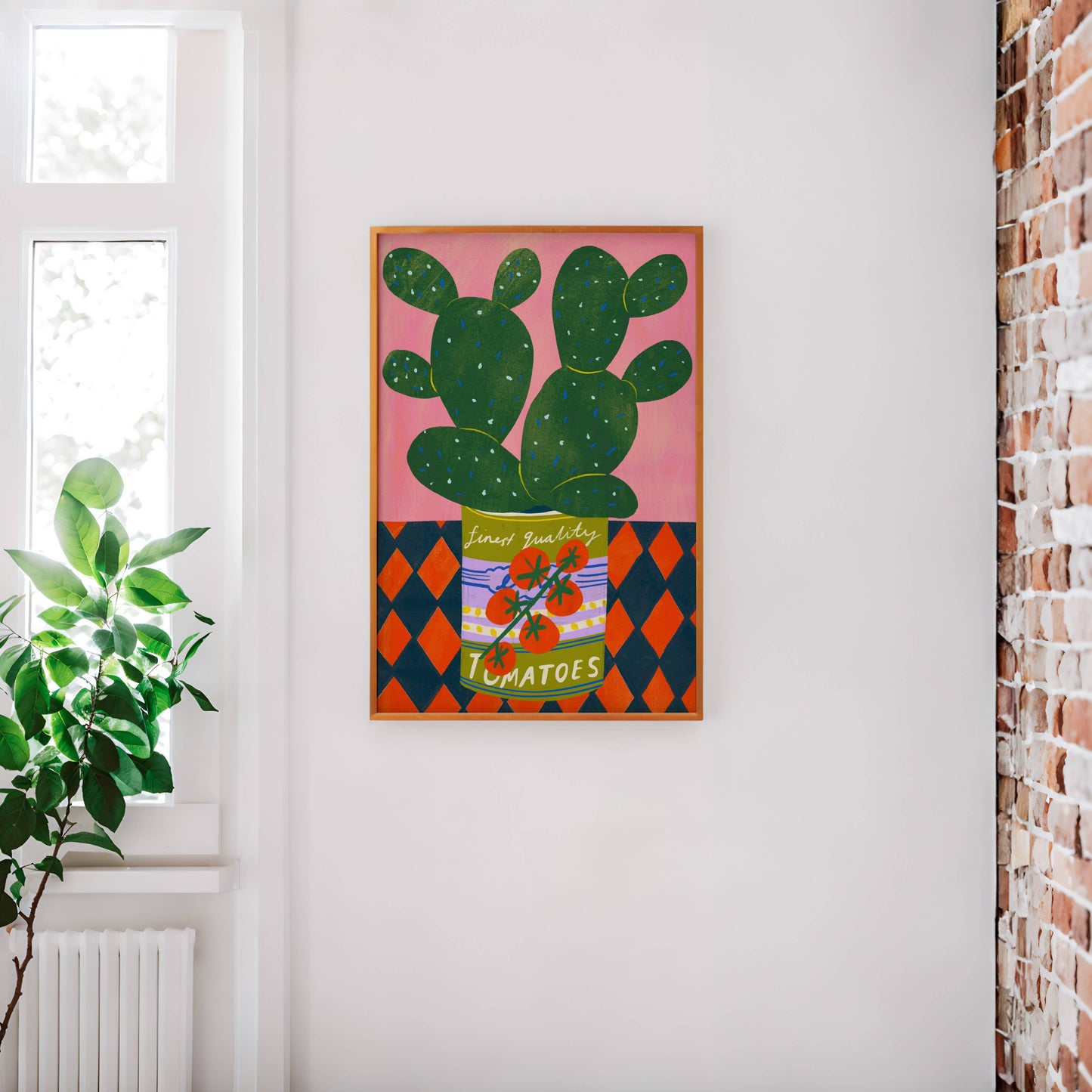 Framed artwork of a cactus on a pink background in a room with a window and plant.