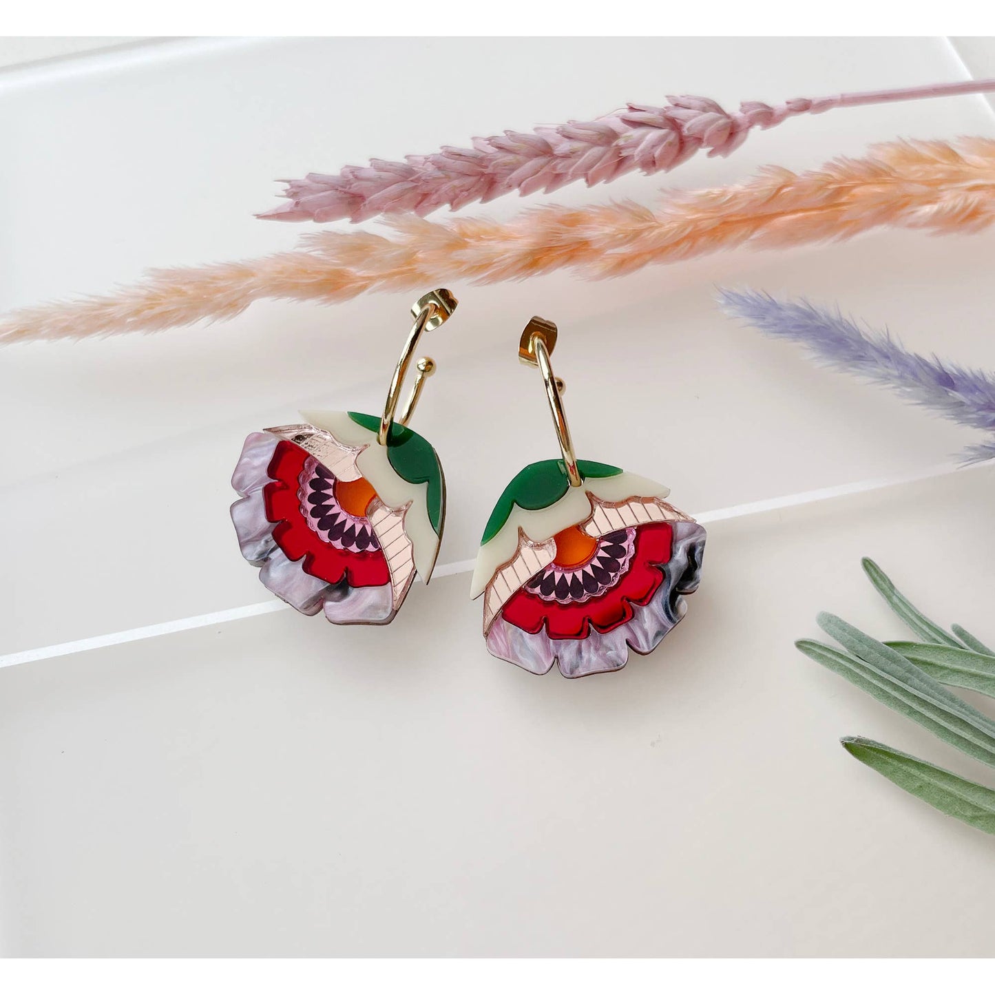 Floral earrings on a white surface with dried lavender and grasses.