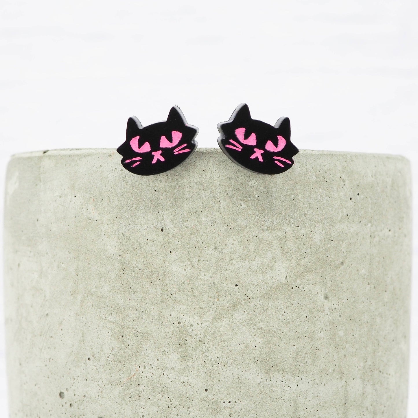 Black cat-shaped earrings with pink accents on a textured surface