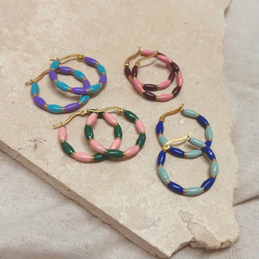 A collection of four candy stripe enamel hoop earrings in different color combinations displayed on a stone surface.