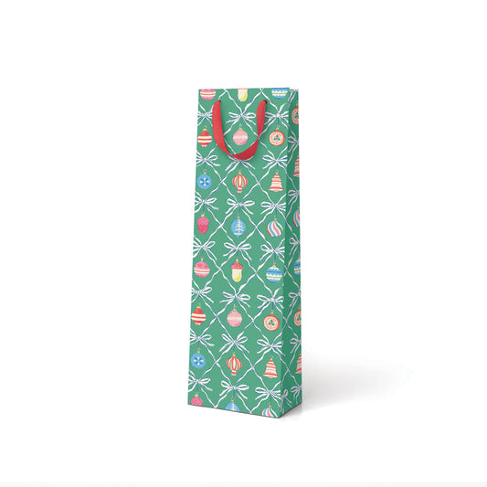 A bottle sized gift bag in green with vintage style decorations illustrated on it, with a red ribbon handle