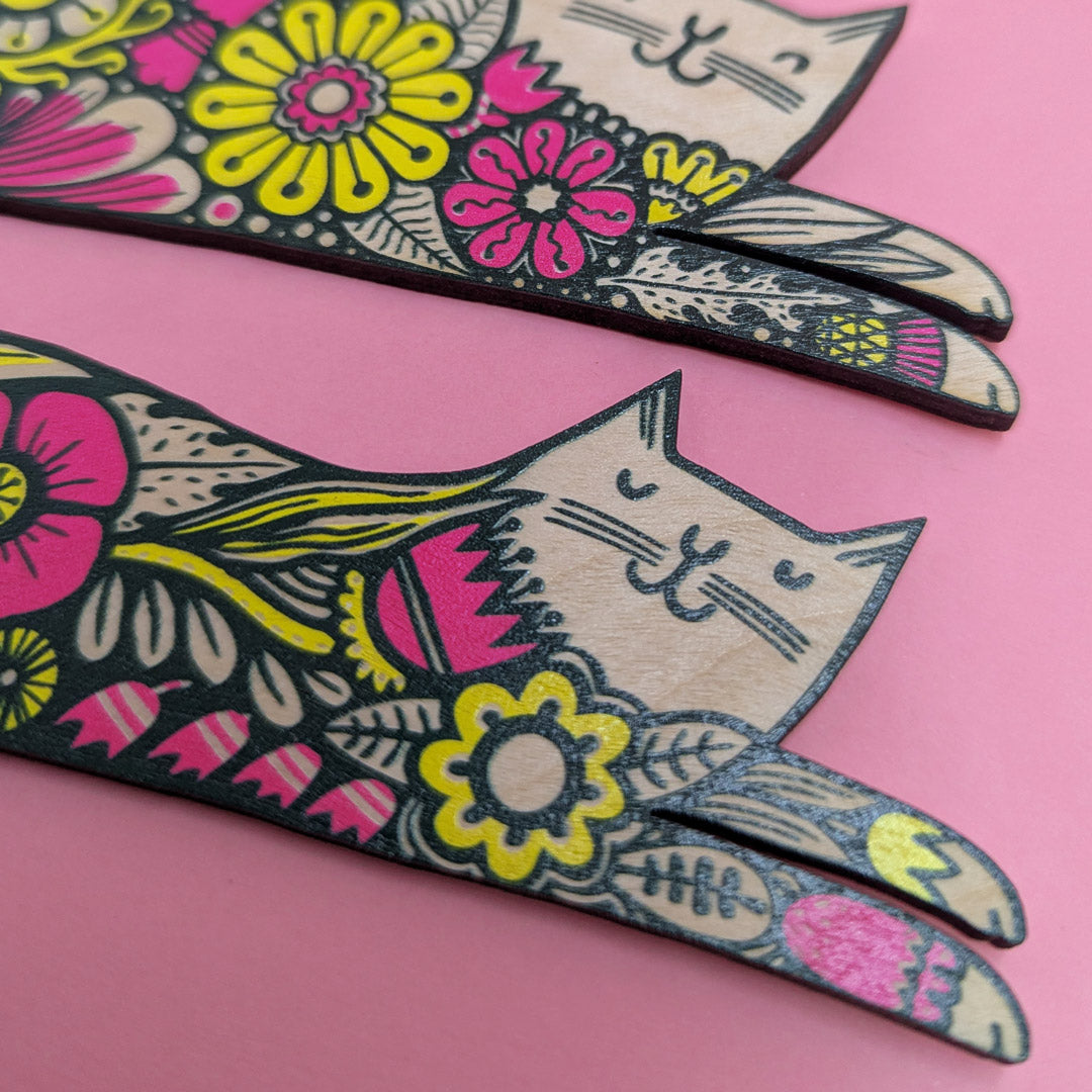 Decorative cat-shaped wall hanging with floral designs on a pink background