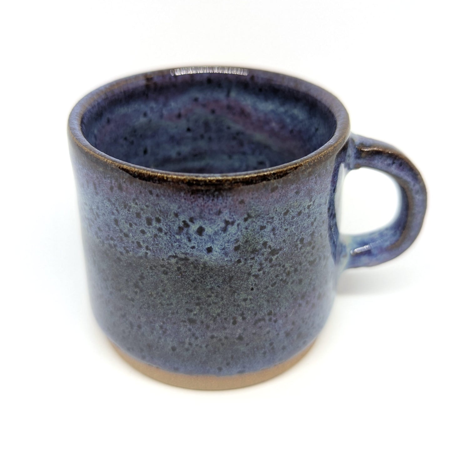 A handcrafted ceramic espresso mug with a purple and blue sunset color palette and a handle on the side, displayed against a neutral background.