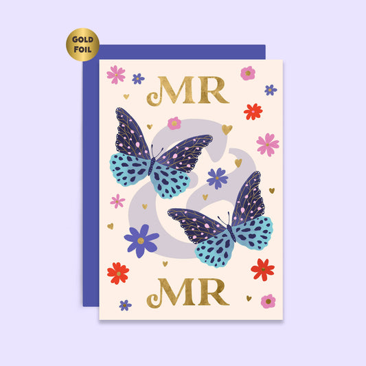 A wedding card with 'MR & MR' text, accompanied by illustrations of butterflies, flowers, and hearts in gold, blue, and multicolor on a beige background. The card also features gold foil details.