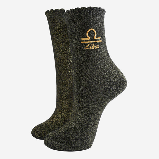 A pair of black socks with gold sparkle and the embroidered gold Libra star sign symbol on the ankle area.