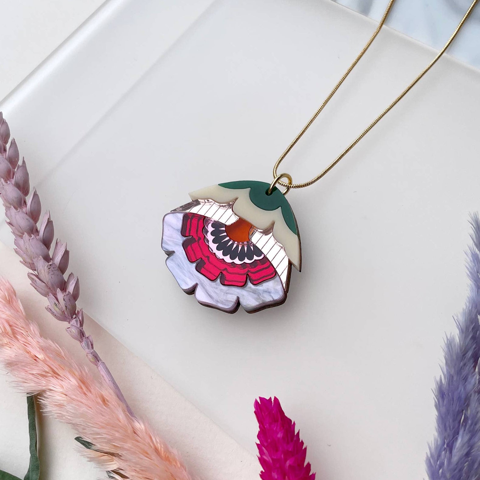 Floral pendant necklace on a white surface with dried plants