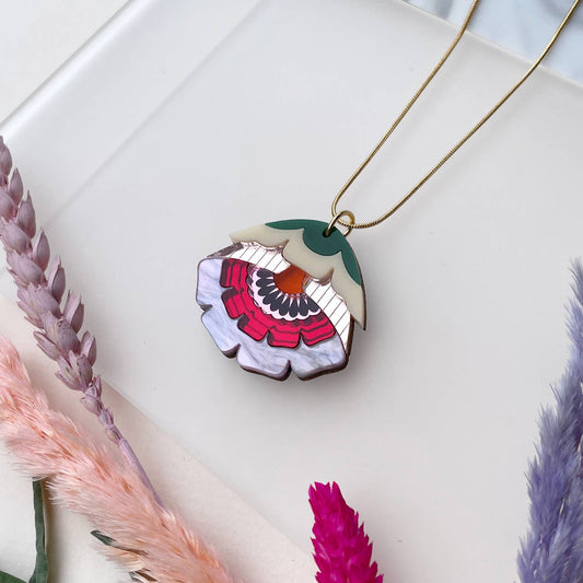 Floral pendant necklace on a white surface with dried plants