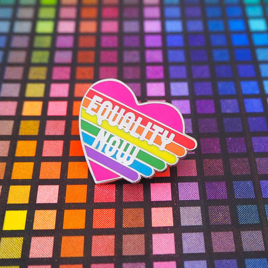 A hard enamel pin with a rainbow heart design and the text 'EQUALITY NOW' in white letters.