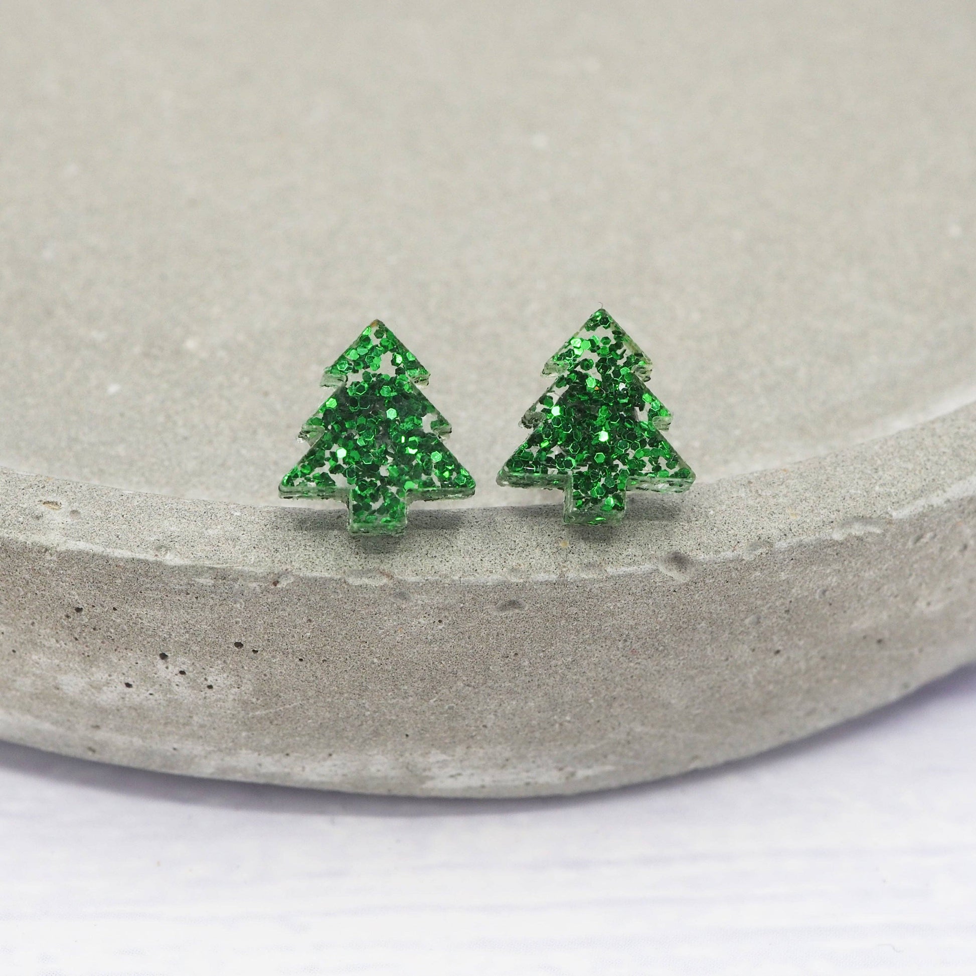 Green tree-shaped earrings on a concrete surface