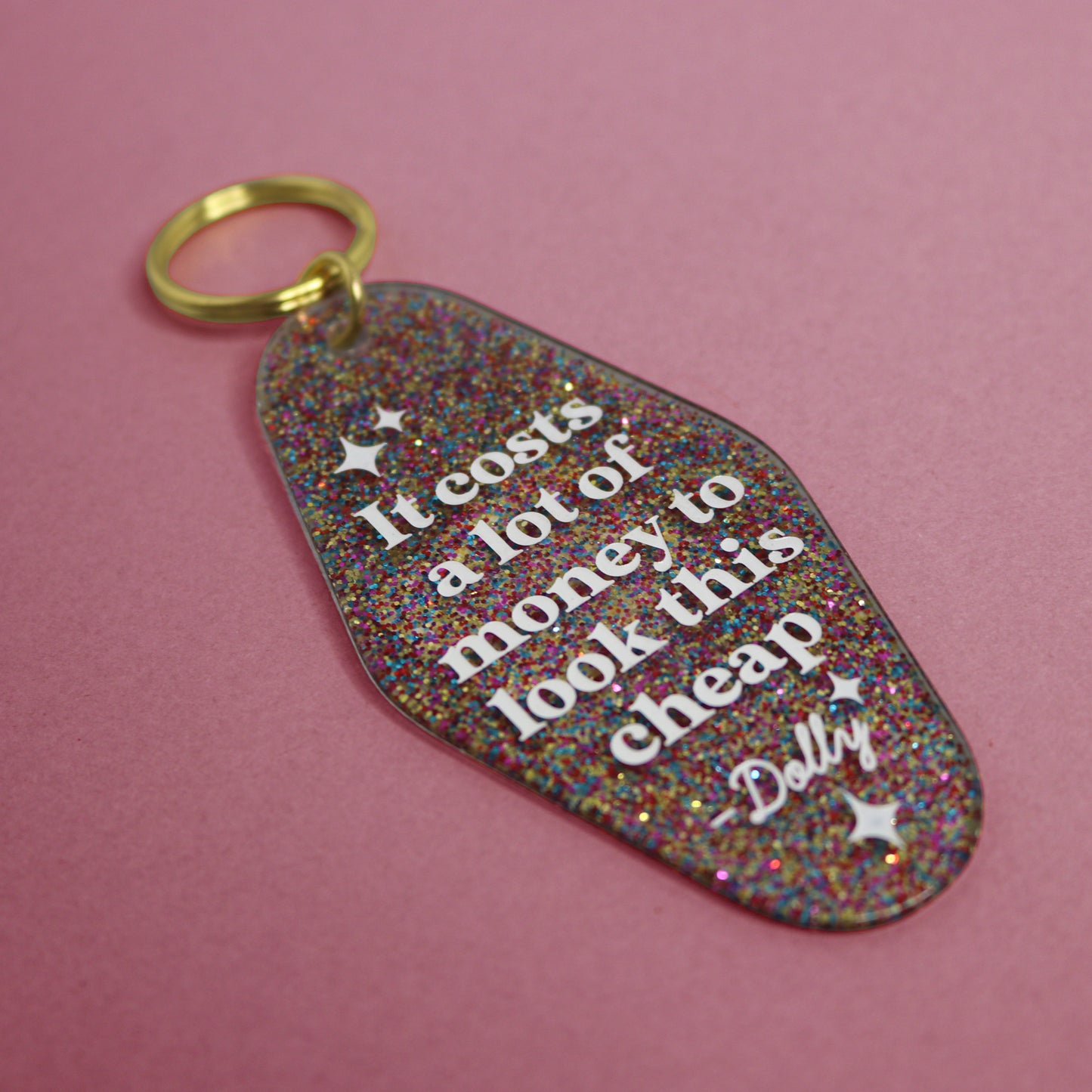 Glittery keychain with text reading "IT COSTS A LOT OF MONEY TO LOOK THIS CHEAP" in a pink background