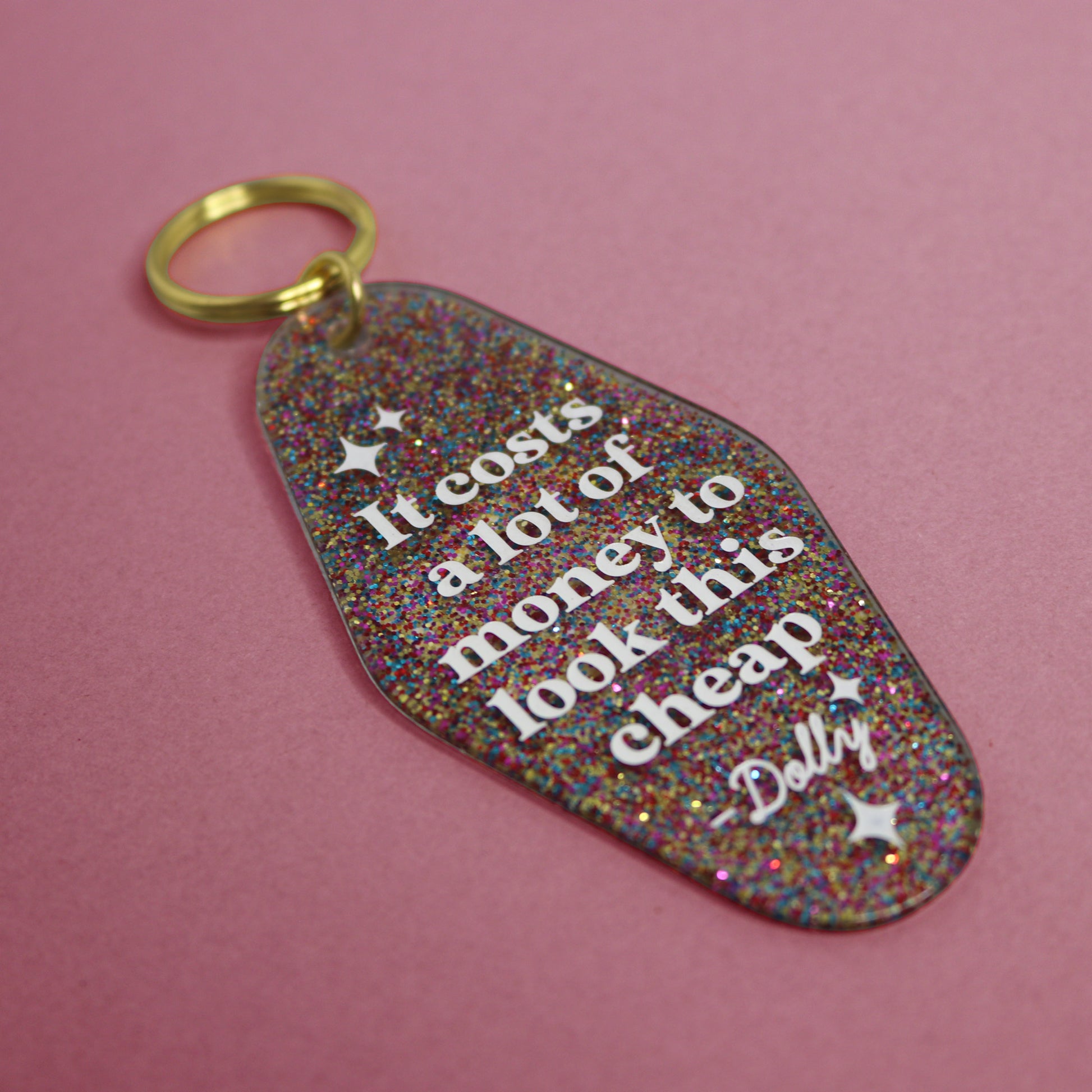 Glittery keychain with text reading "IT COSTS A LOT OF MONEY TO LOOK THIS CHEAP" in a pink background