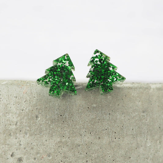Green glittery Christmas tree earrings on a concrete surface with a white background