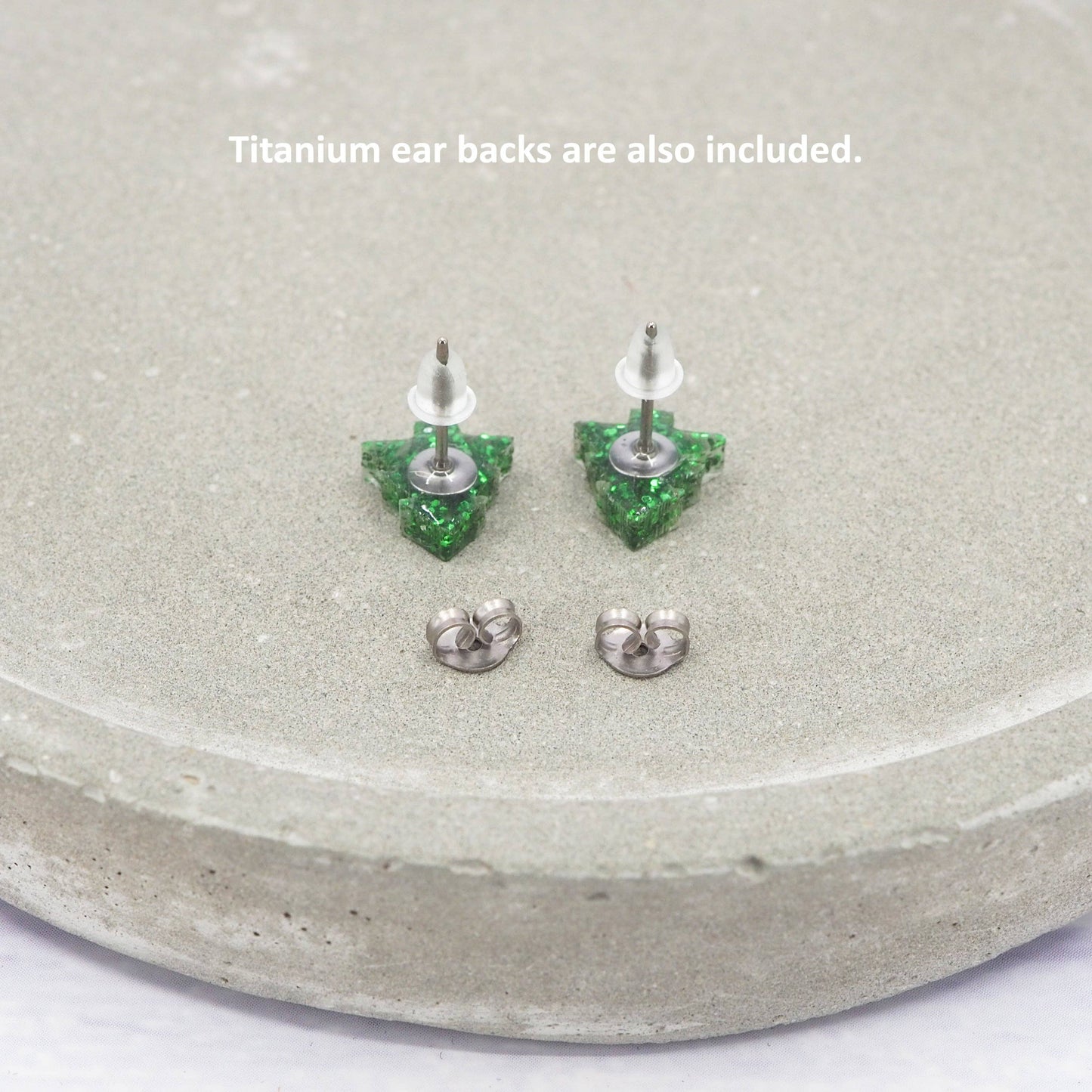 Green crystal earrings on a gray surface with text about titanium ear backs.