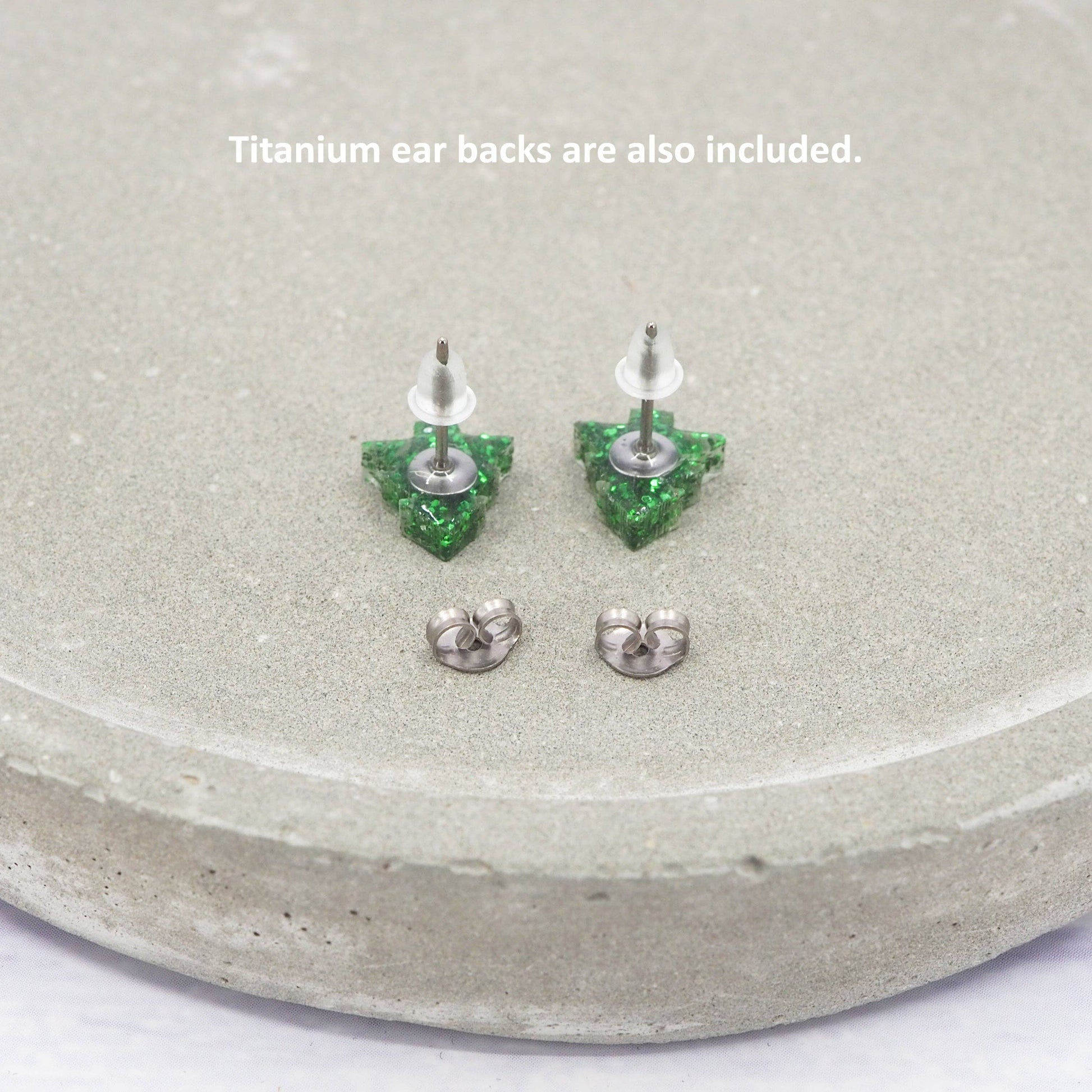Green crystal earrings on a gray surface with text about titanium ear backs.