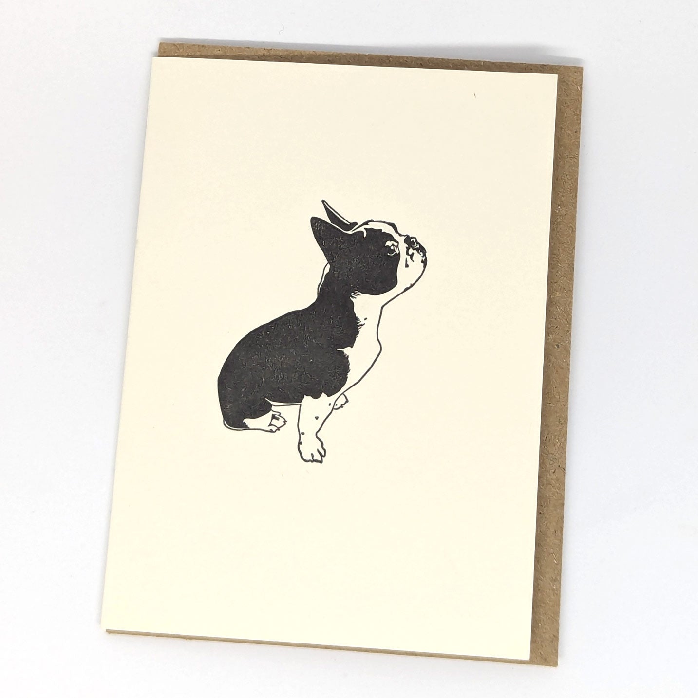 A greeting card featuring a letterpress illustration of a French Bulldog, with a beige background and a brown envelope.