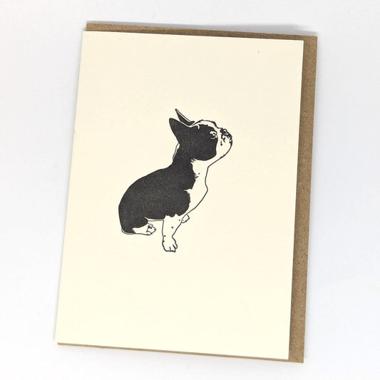 A greeting card featuring a letterpress illustration of a French Bulldog, with a beige background and a brown envelope.