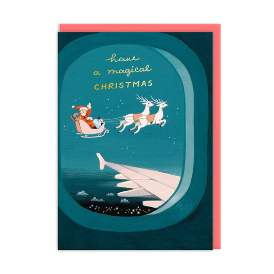 A christmas greeting card that reads 'have a magical christmas' in gold foil. Illustration shows Santa and his reindeer lying next to an airplane as viewed from the plane window, has a distinctive retro illustration style.