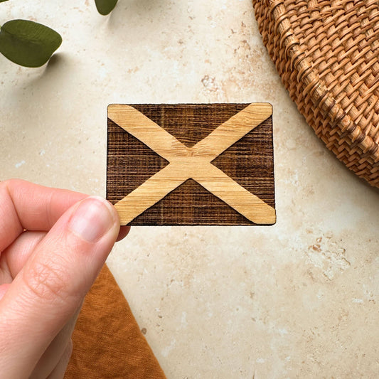A hand holding a wooden magnet with a hand-drawn Scottish flag burnt onto it