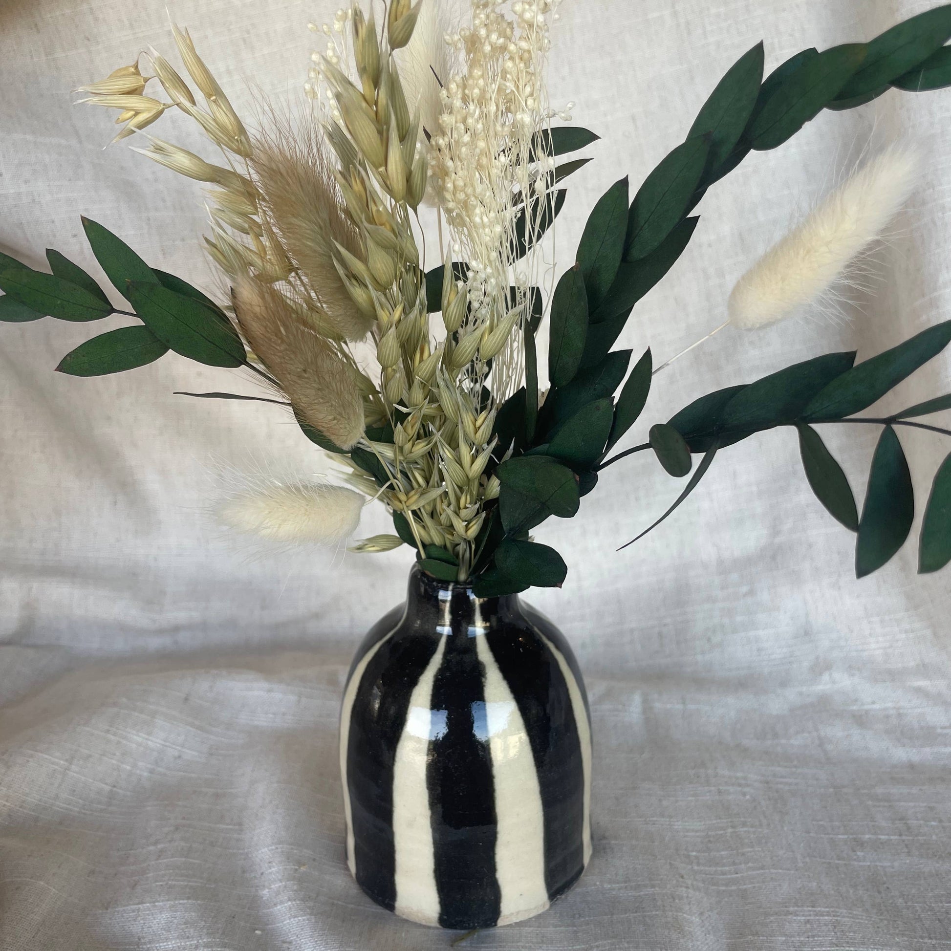 Black and white striped vase with dried flowers on a textured fabric background