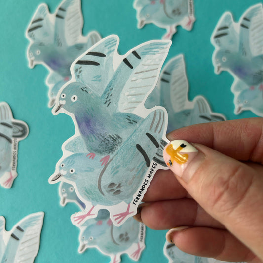 Hand holding a sticker of two pigeons - one standing on top of the other's back.