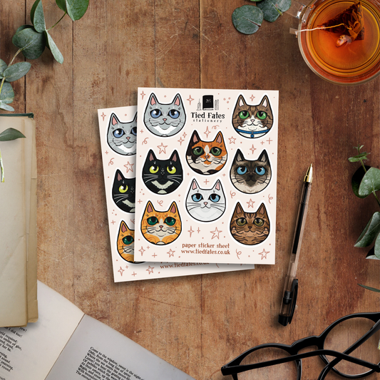 Sheet of cat-themed stickers on a wooden surface with a pen and glasses.