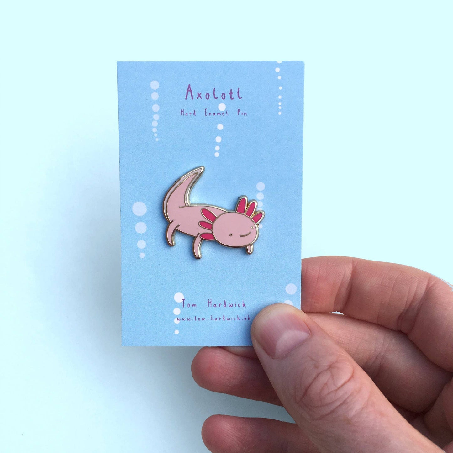 Axolotl pin on a blue card held by a hand against a light blue background