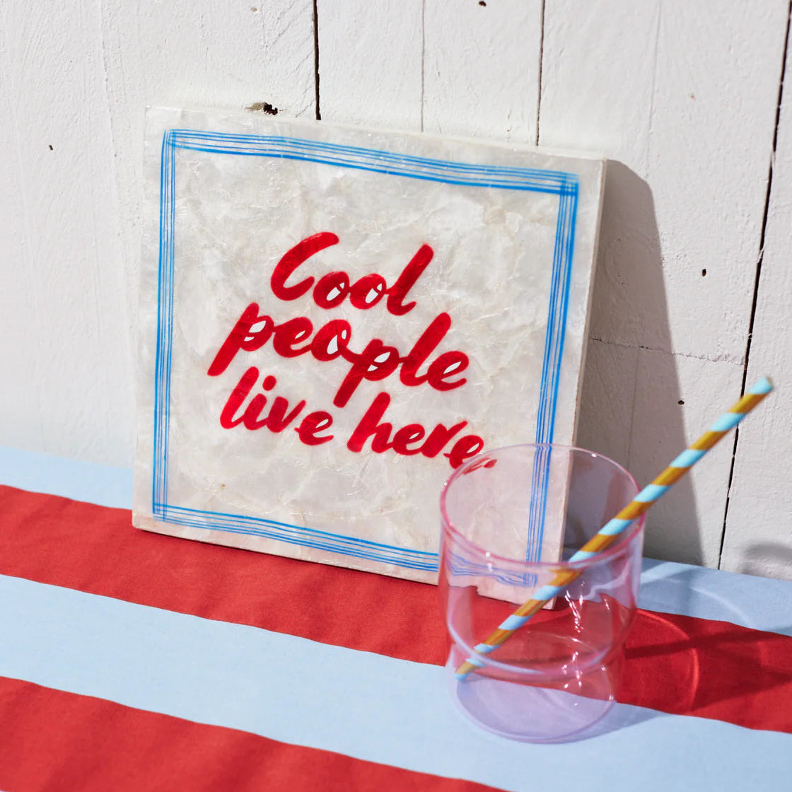 Decorative sign with 'Cool people live here' text on a table with a glass and straw.