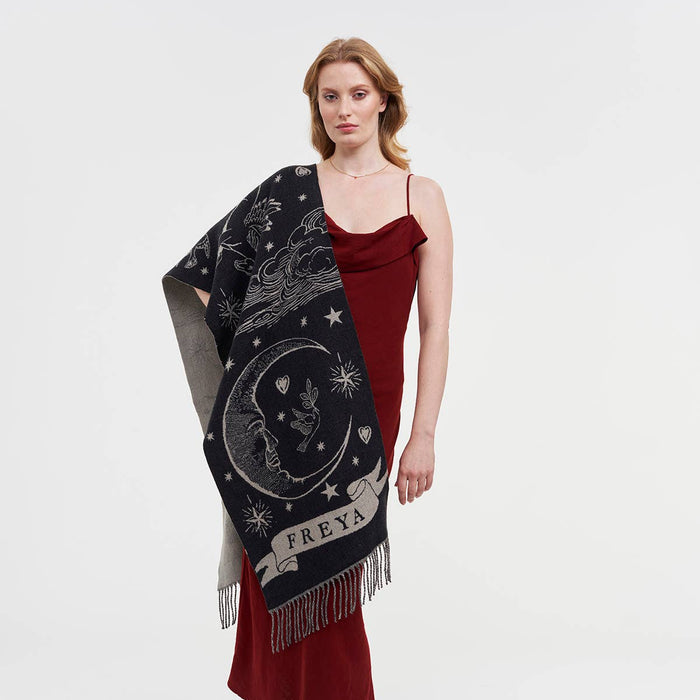 Woman in a red dress wearing a large black and white woven scarf with a crescent moon and a banner with the word Freya on it.