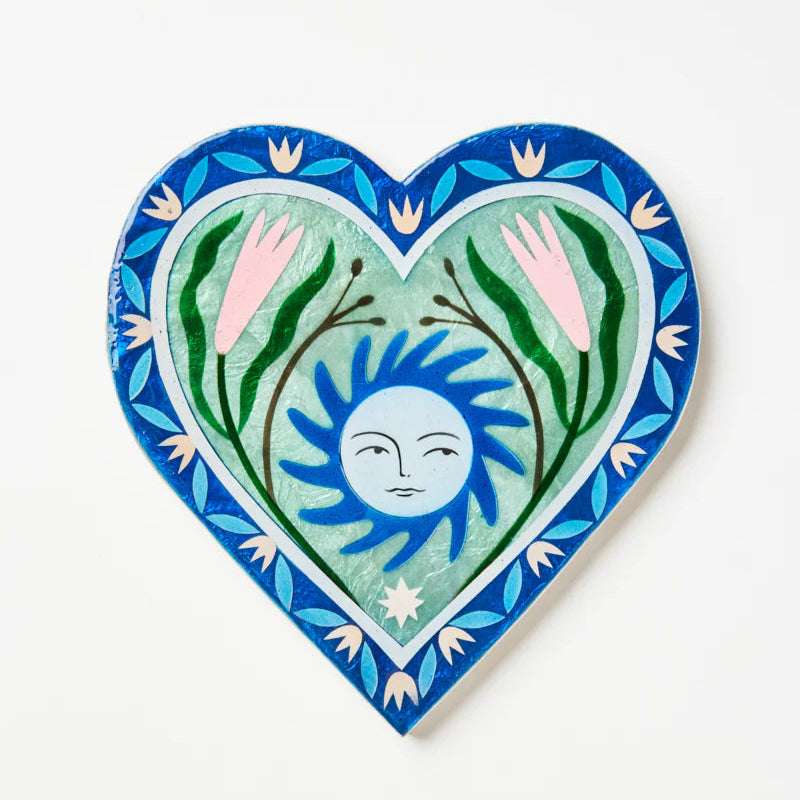 Heart-shaped decorative tile with a sun and plant design on a white background