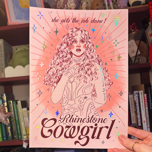 Poster of a 'Rhinestone Cowgirl' design held in front of a bookshelf.