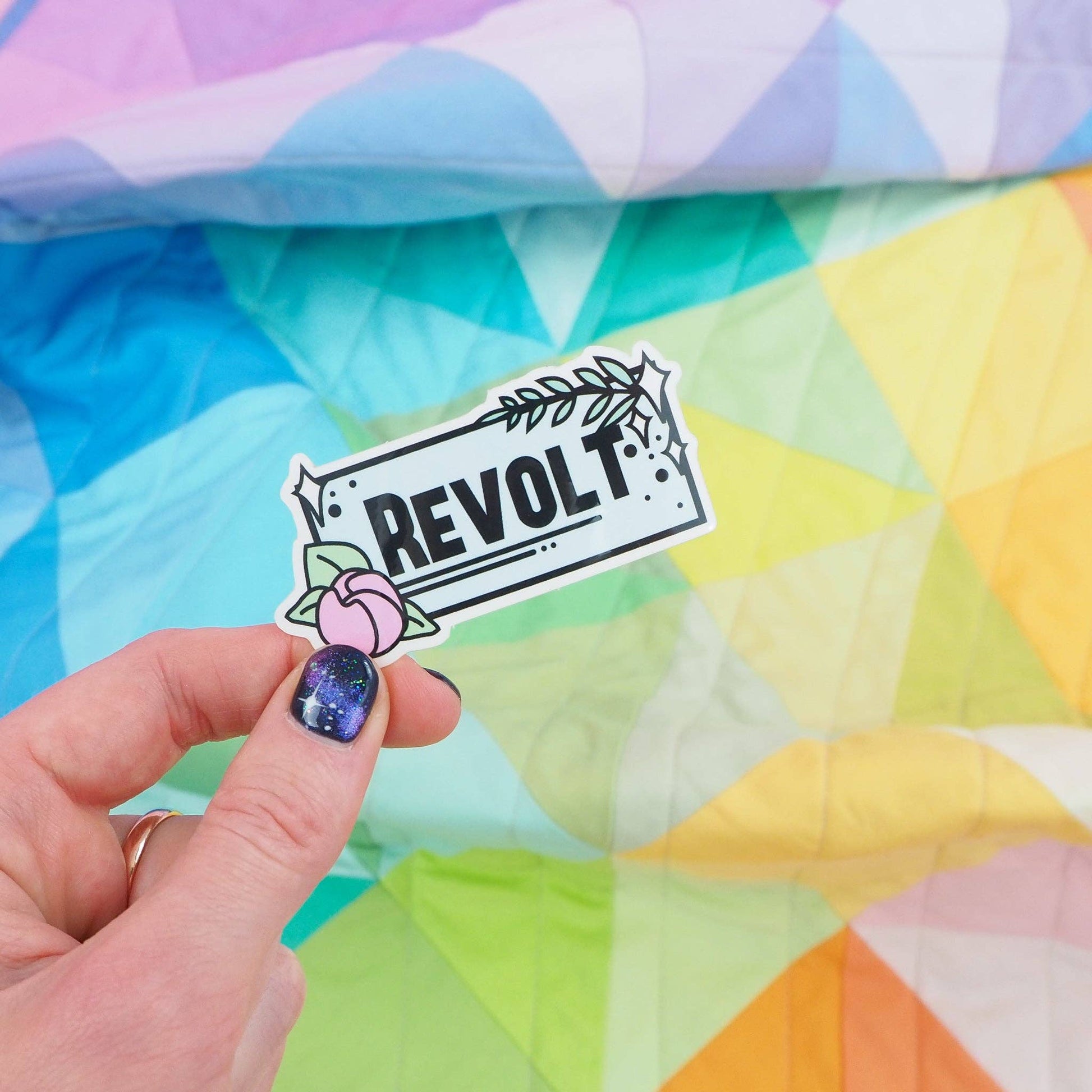 A person holding a vinyl sticker with the word 'REVOLT' displayed against a colorful geometric pattern background.