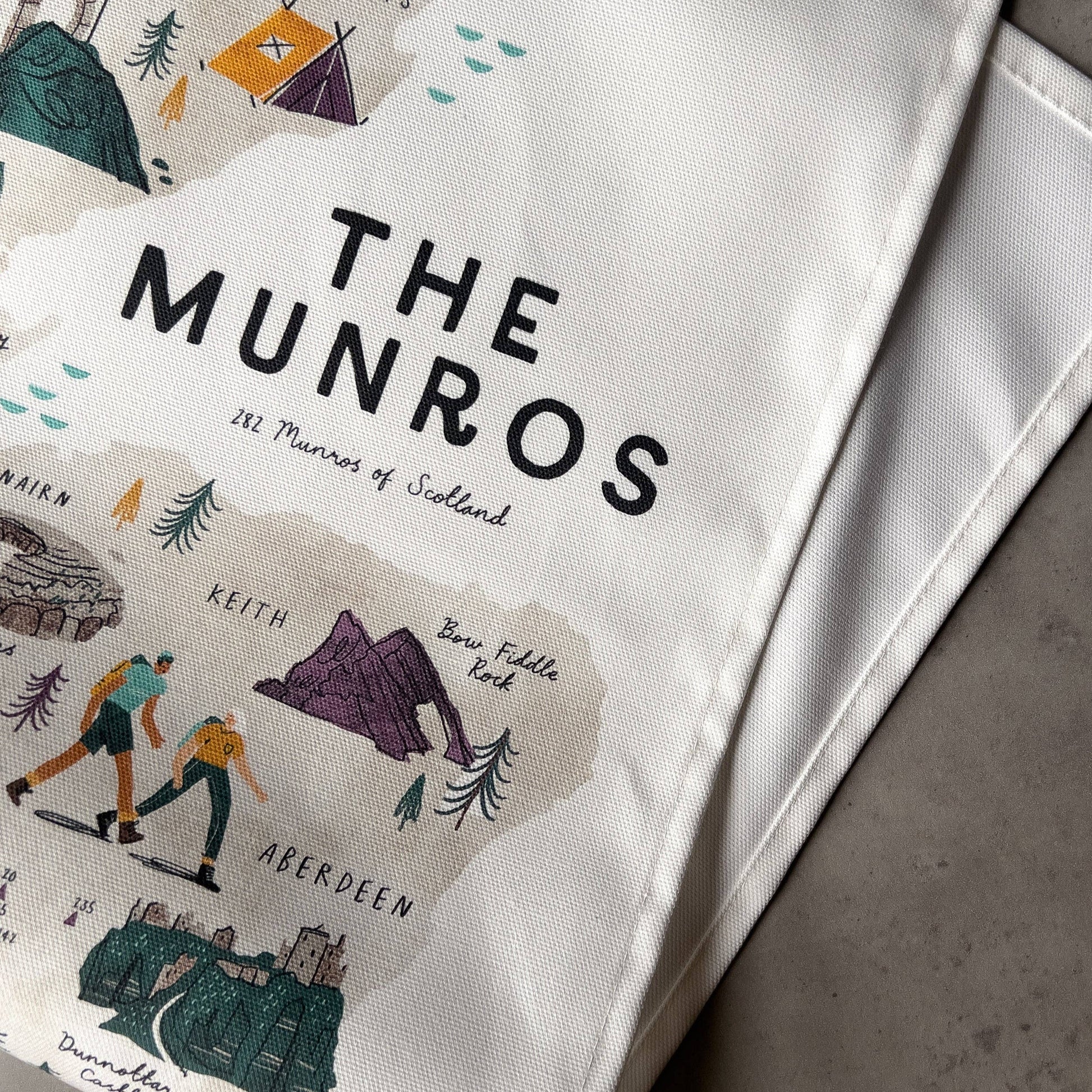 White teatowel with 'The Munros' branding and illustrations on a gray surface