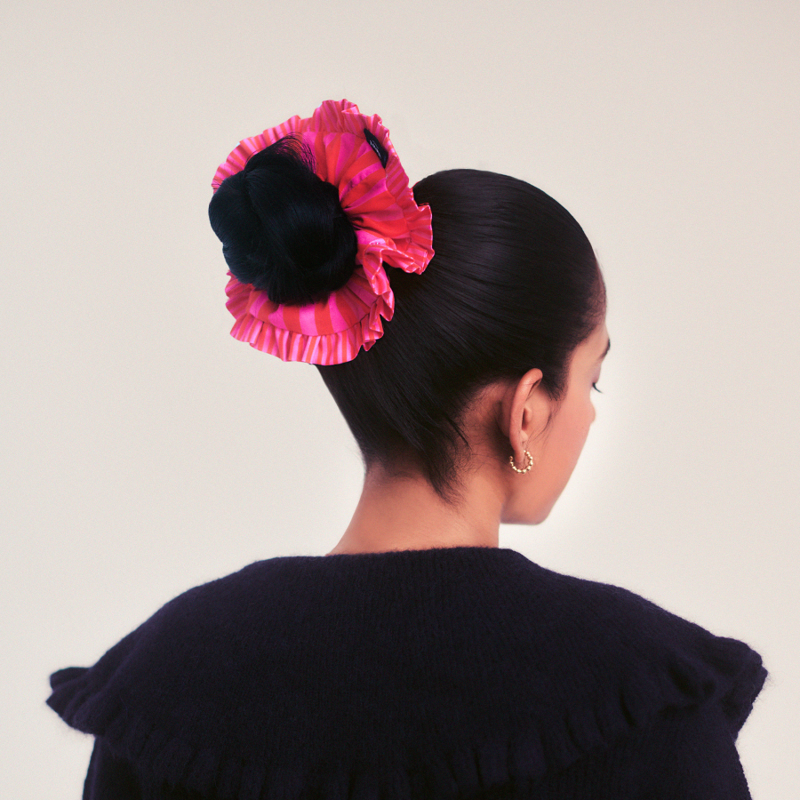 Woman with a pink hair scrunchie and black hair against a plain background