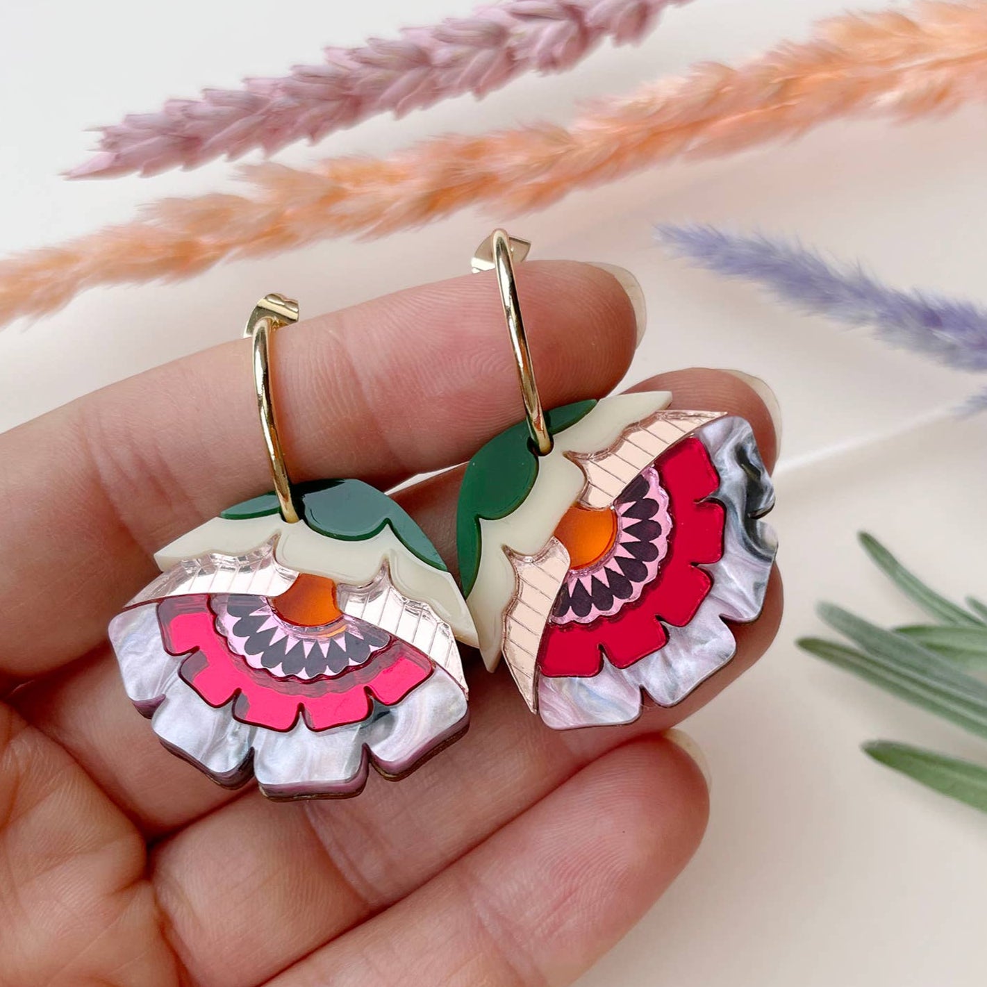 Colorful floral earrings held in a hand with a soft background