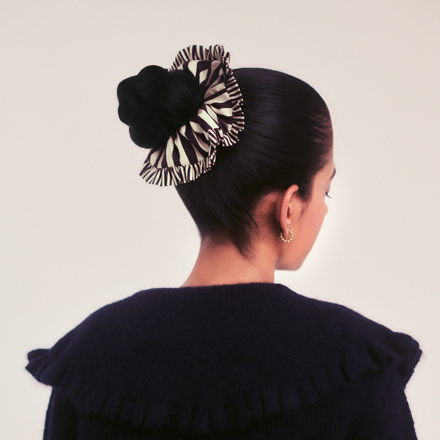 Woman with a stylish hair bun featuring a striped hair accessory against a plain background
