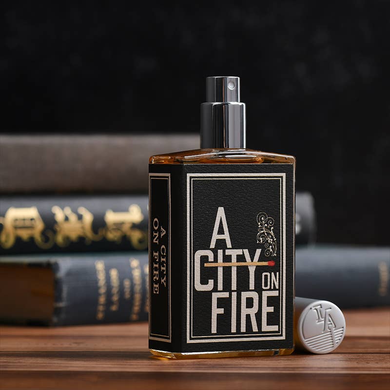Perfume bottle labeled 'A City on Fire' with books in the background