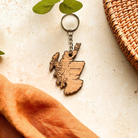 A wooden keyring in the shape of a Scotland map, displayed on a beige background 