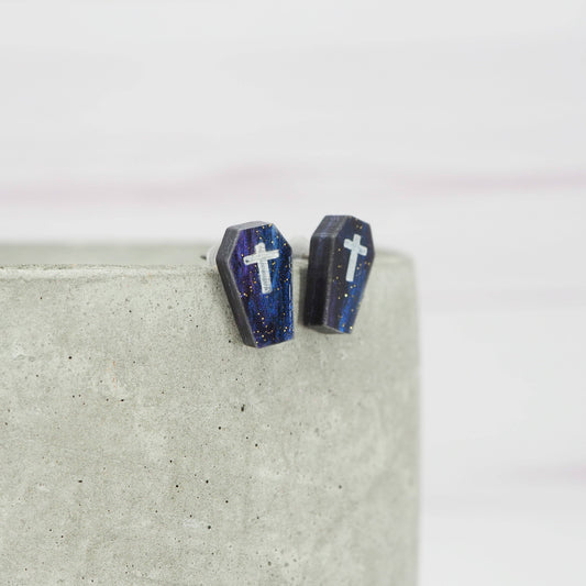 Coffin-shaped earrings with cross details on a light gray surface